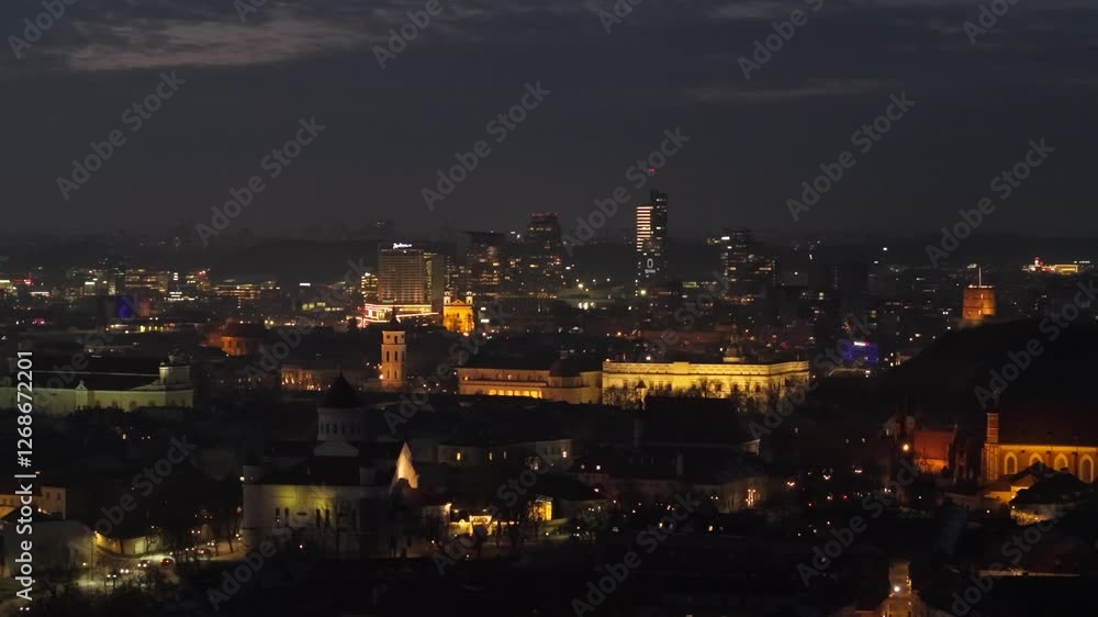Illuminated night view of Vilnius, Lithuania, showcasing a blend of historic landmarks and modern skyscrapers in the cityscape. Illuminated night view of Vilnius, Lithuania, showcasing a blend of historic landmarks and modern skyscrapers in the cityscape.