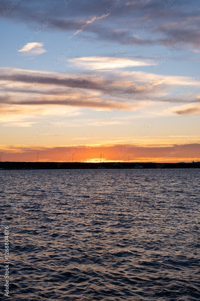 Naklejka premium Beautiful golden sunrise over a calm sea with distant horizon. Peaceful sunrise scene with the sun reflecting on calm water. Early morning at bay