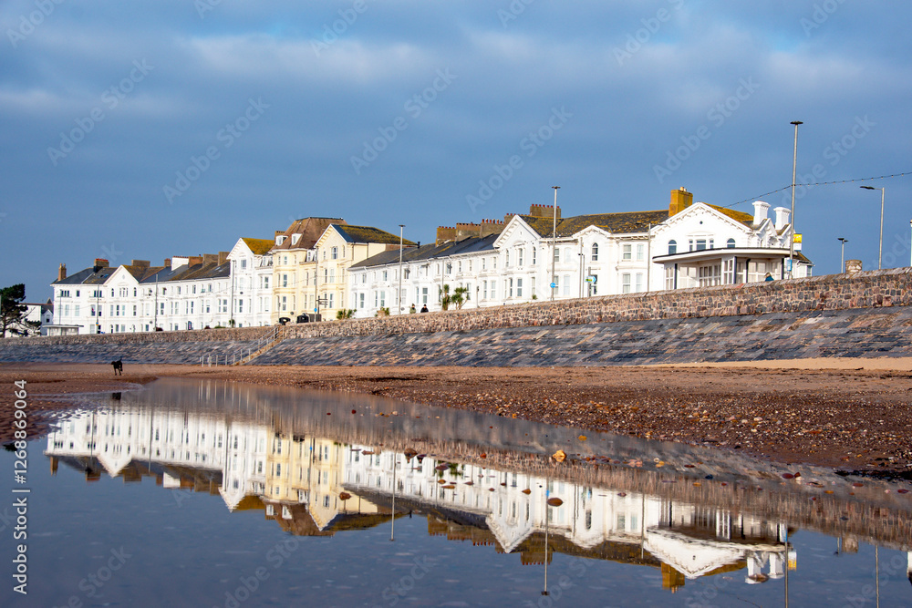 Obraz premium Seaside properties, homes and houses with a strong reflection in standing water on a beach. Seafront scene and lifestyle picture. Retirement homes and coastal living. Estate agent.