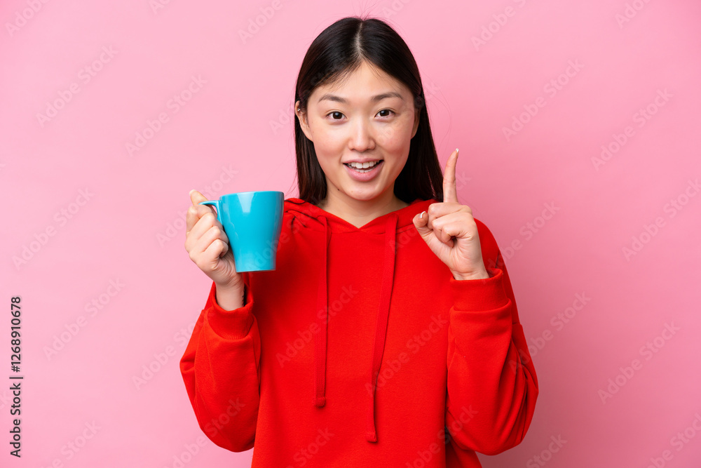 Young Chinese woman holding cup of coffee isolated on pink background pointing up a great idea Young Chinese woman holding cup of coffee isolated on pink background pointing up a great idea