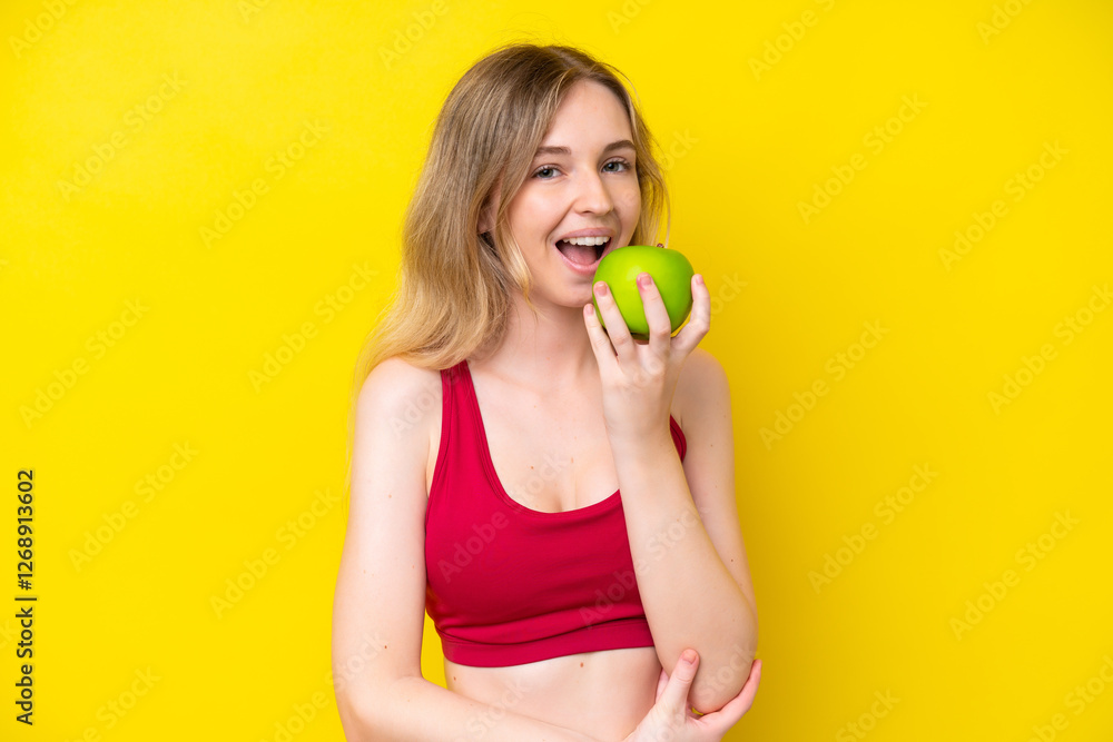 Blonde English young girl isolated on yellow background eating an apple Blonde English young girl isolated on yellow background eating an apple