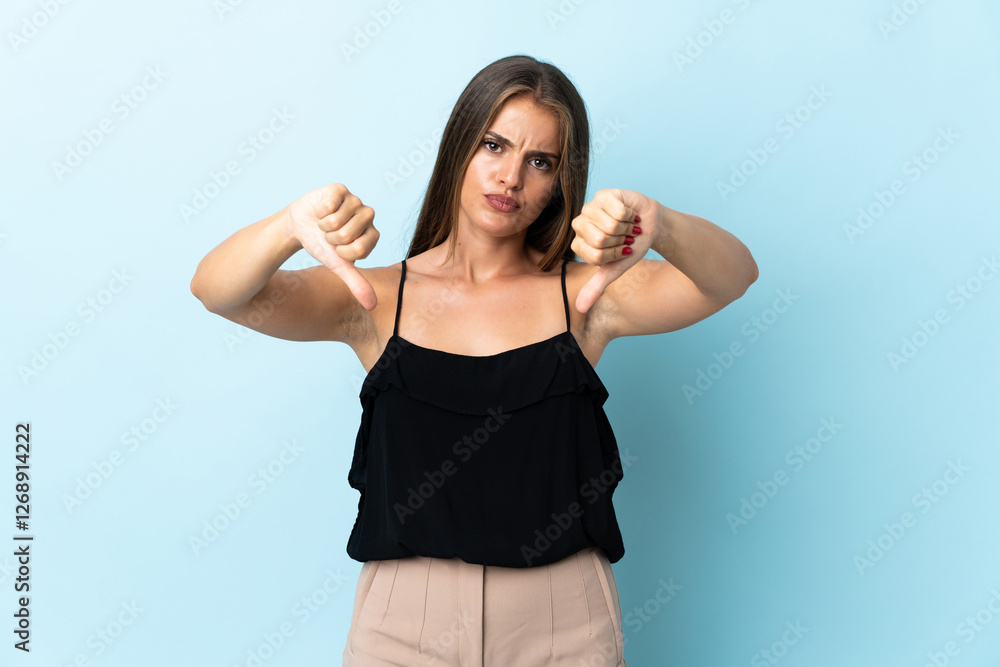 Fototapeta premium Young Uruguayan woman isolated on blue background showing thumb down with two hands