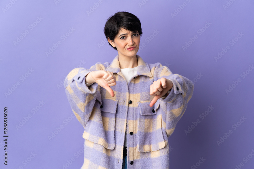 Woman with short hair isolated on purple background showing thumb down with two hands Woman with short hair isolated on purple background showing thumb down with two hands