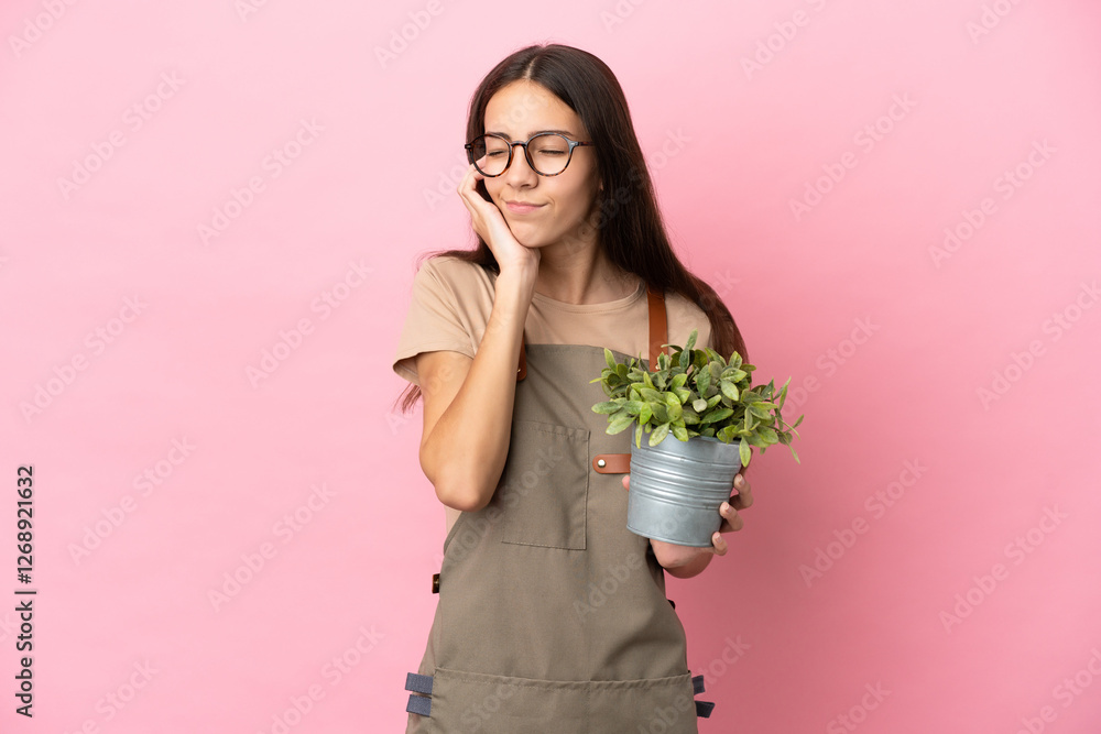 Young gardener girl holding a plant isolated on pink background frustrated and covering ears Young gardener girl holding a plant isolated on pink background frustrated and covering ears