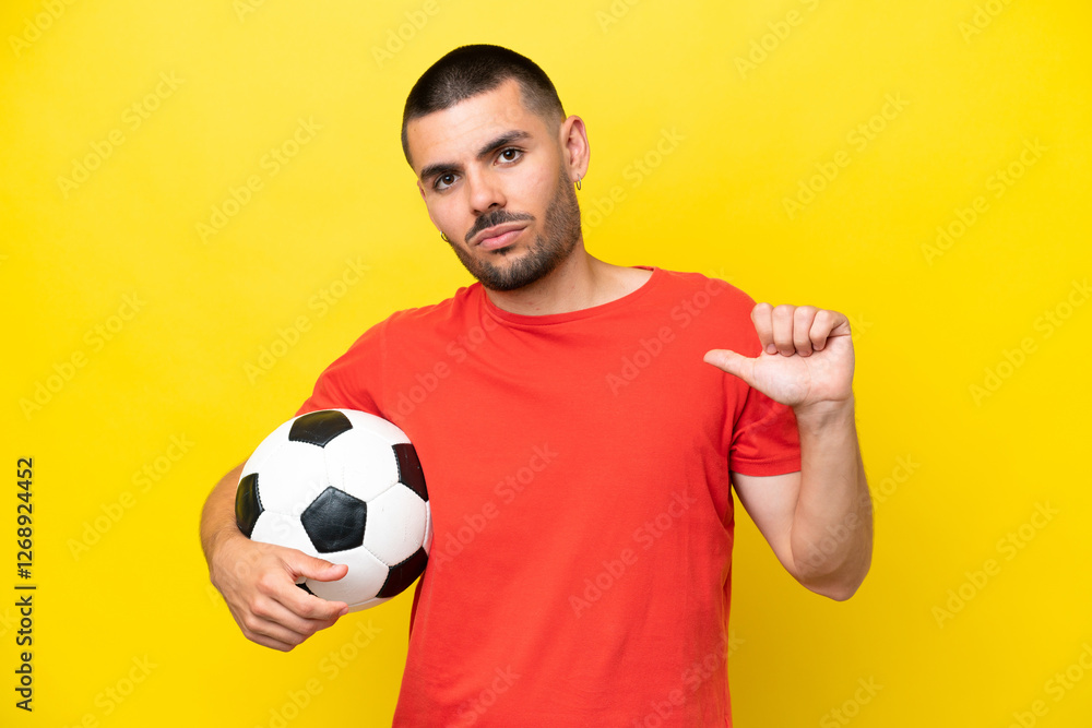 Young caucasian man playing soccer isolated on yellow background proud and self-satisfied
