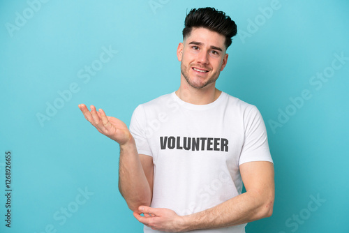 Young volunteer caucasian man isolated on blue background extending hands to the side for inviting to come