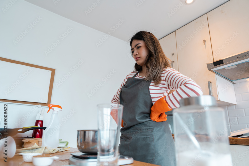 Woman in apron and gloves looking serious at messy kitchen counter Woman in apron and gloves looking serious at messy kitchen counter