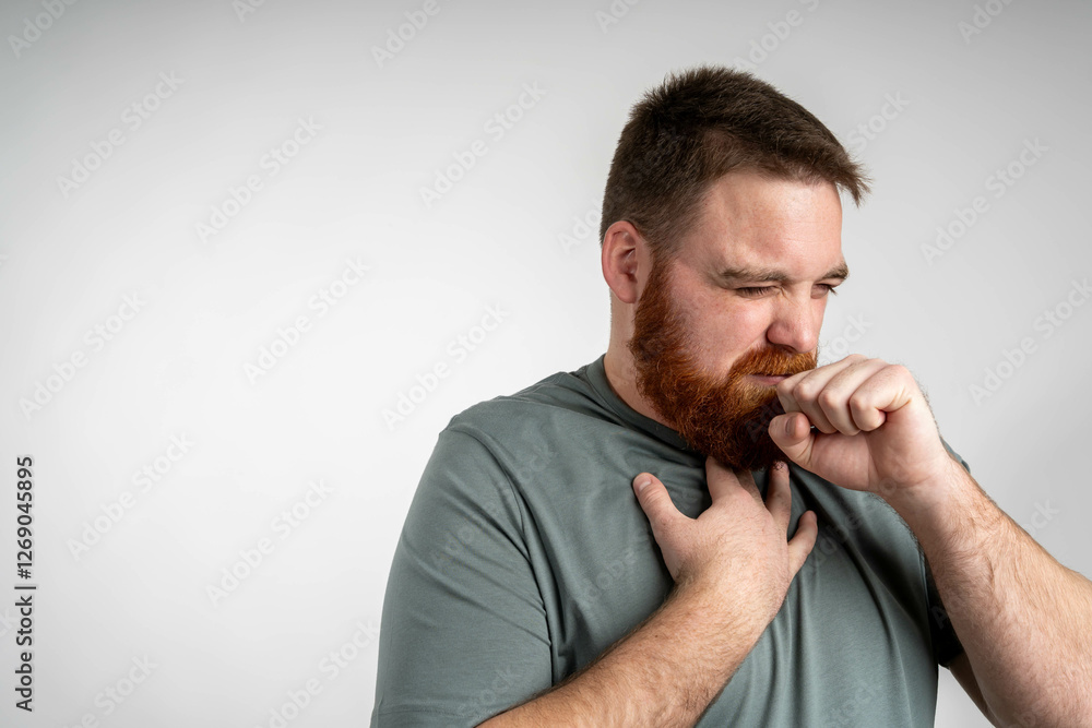 Young bearded man coughing over isolated blue background. Young man over grey wall is suffering with cough and feeling bad. Young bearded man coughing over isolated blue background. Young man over grey wall is suffering with cough and feeling bad.
