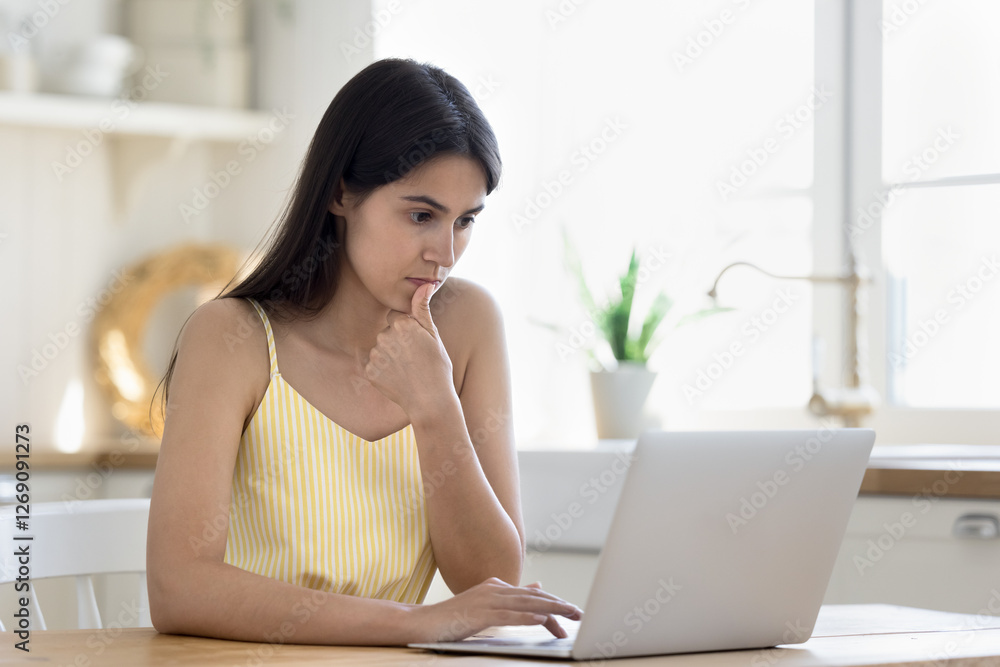 Focused on screen. Pensive generation z woman working studying remotely use notebook at home office concentrated on searching information online analyze statistic data choose education video to watch Focused on screen. Pensive generation z woman working studying remotely use notebook at home office concentrated on searching information online analyze statistic data choose education video to watch