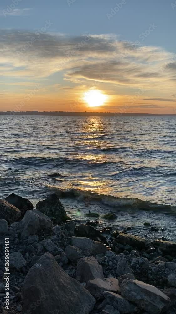 Sunset over calm ocean waves at coastal rocks with vibrant sky colors in the evening Sunset over calm ocean waves at coastal rocks with vibrant sky colors in the evening