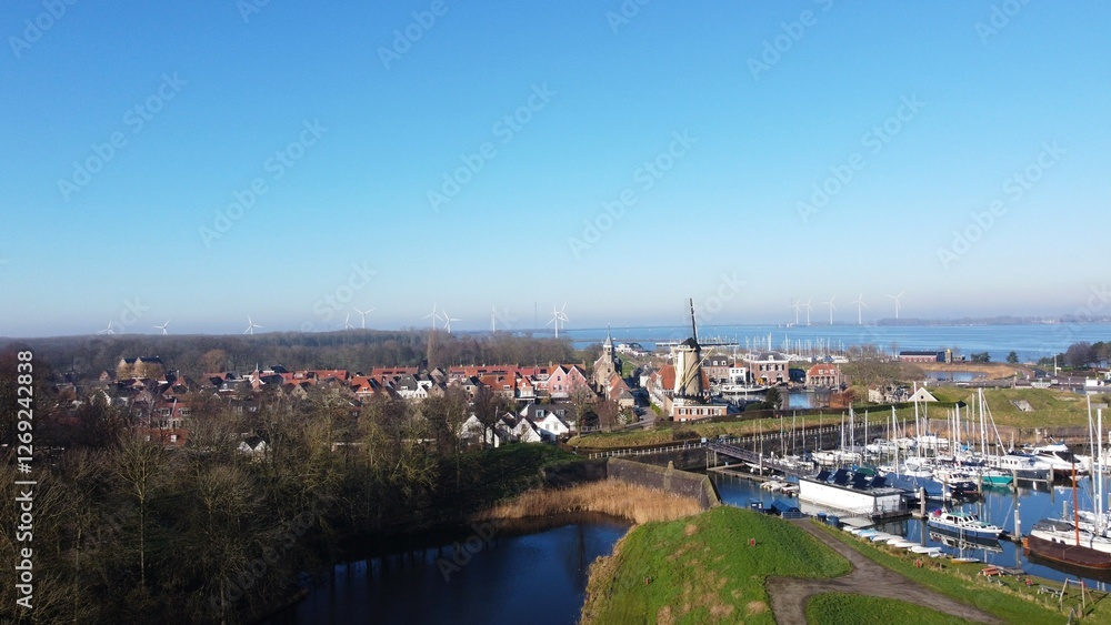 Fototapeta premium A park image in the Netherlands. An autumn season with bare trees and a walking path. A well-trodden path that leads to the water of a lake and a view of Willemstad with the mill of the village.