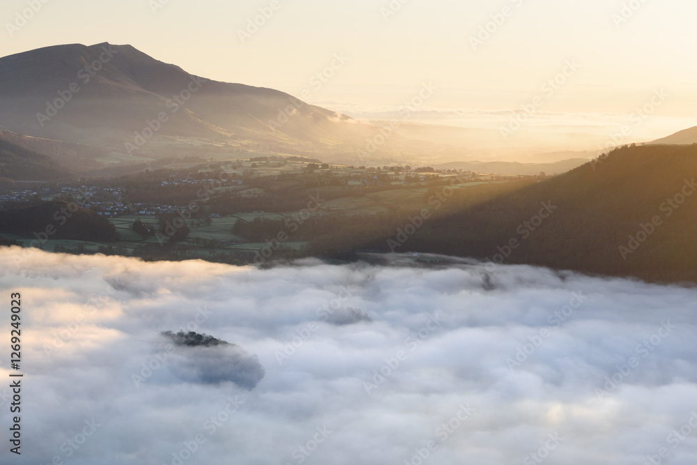 Obraz premium Golden spring sunlight on Blencathra mountain overlooking calm misty Derwentwater, Lake District, UK.