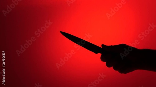 Silhouette of hand holding knife on red background