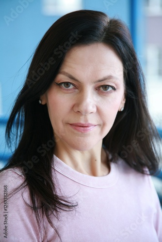 Portrait of an attractive 51 year old woman with nude makeup and black eyeliner wearing a pink ribbed long sleeve and looking at the camera
