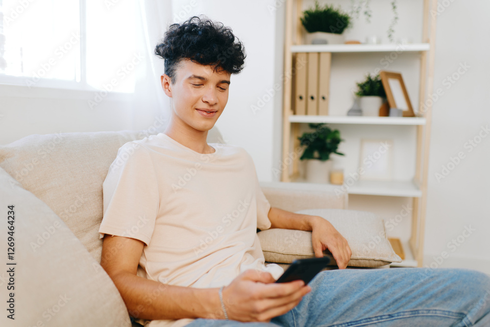Young man relaxing at home checking phone, casual attire, cozy interior with plants Young man relaxing at home checking phone, casual attire, cozy interior with plants