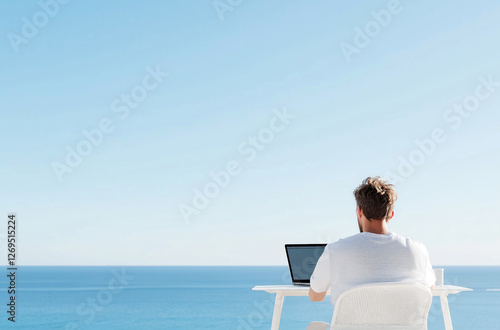 Man working remotely with laptop by the ocean under clear blue sky
