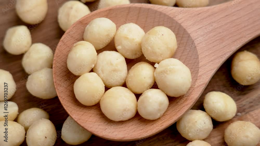 Roasted macadamia nuts in a wooden spoon on rustic background. Nutrient snack with healthy fats and antioxidants. Top view. Rotation