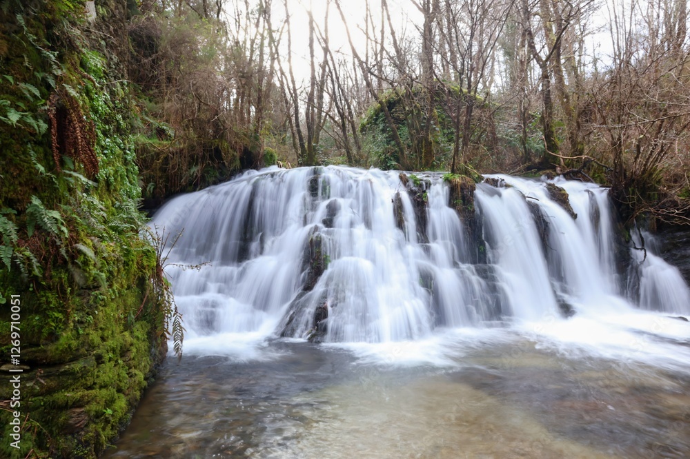 Fototapeta premium Paisaje de cascada de agua efecto seda con molino de piedra al fondo y detalle en primer plano de muro de piedra con musgo 