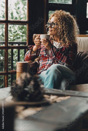 Foto Mature woman sitting alone at home holding a cup of hot herbal tea while looking