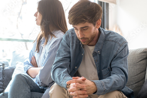 Unhappy couple sitting on a couch at home, avoiding eye contact, engaged in a tense discussion about marriage issues, trust problems, emotional detachment, financial difficulties, and separation