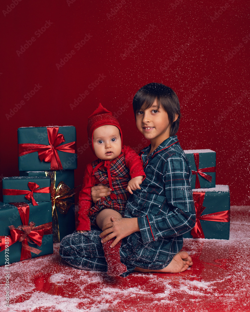 brother and sister are sitting on the floor among green New Year gift boxes on a red background with snow.