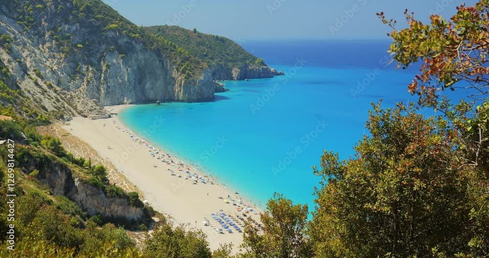 The picturesque Mylos beach in Lefkada island, with turquoise waters of the Mediterranean sea washing the white pebbled shore, framed by high rock cliffs covered green lush vegetation and pine trees The picturesque Mylos beach in Lefkada island, with turquoise waters of the Mediterranean sea washing the white pebbled shore, framed by high rock cliffs covered green lush vegetation and pine trees