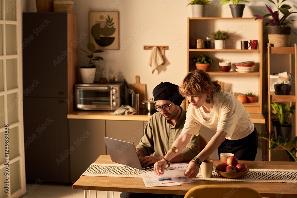 Two colleagues working at a kitchen counter, discussing documents and ideas in a cozy, modern home setting with plants and shelves filled with various items Two colleagues working at a kitchen counter, discussing documents and ideas in a cozy, modern home setting with plants and shelves filled with various items