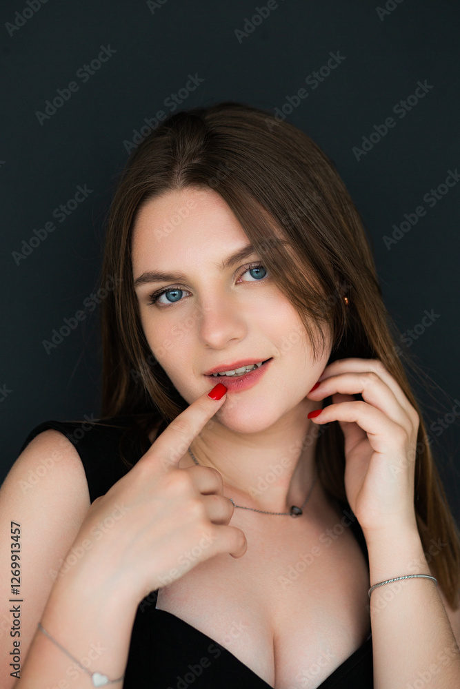 A woman poses against a dark background, touching her head with one hand and her lips with the other. Her nails are painted with red polish. The facial expression is calm and thoughtful. A woman poses against a dark background, touching her head with one hand and her lips with the other. Her nails are painted with red polish. The facial expression is calm and thoughtful.