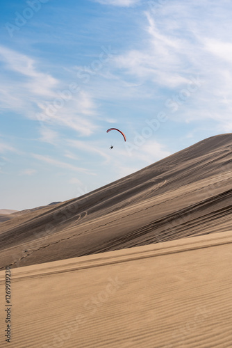 Lot paralotnią nad pustynną wydmą w bezchmurnym niebie
