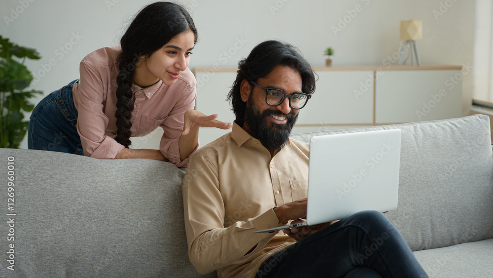 Arabian Indian couple on couch sofa use computer laptop shopping online internet store happy multiracial wife husband smiling lovely customers woman and man search goods purchase on website at home Arabian Indian couple on couch sofa use computer laptop shopping online internet store happy multiracial wife husband smiling lovely customers woman and man search goods purchase on website at home