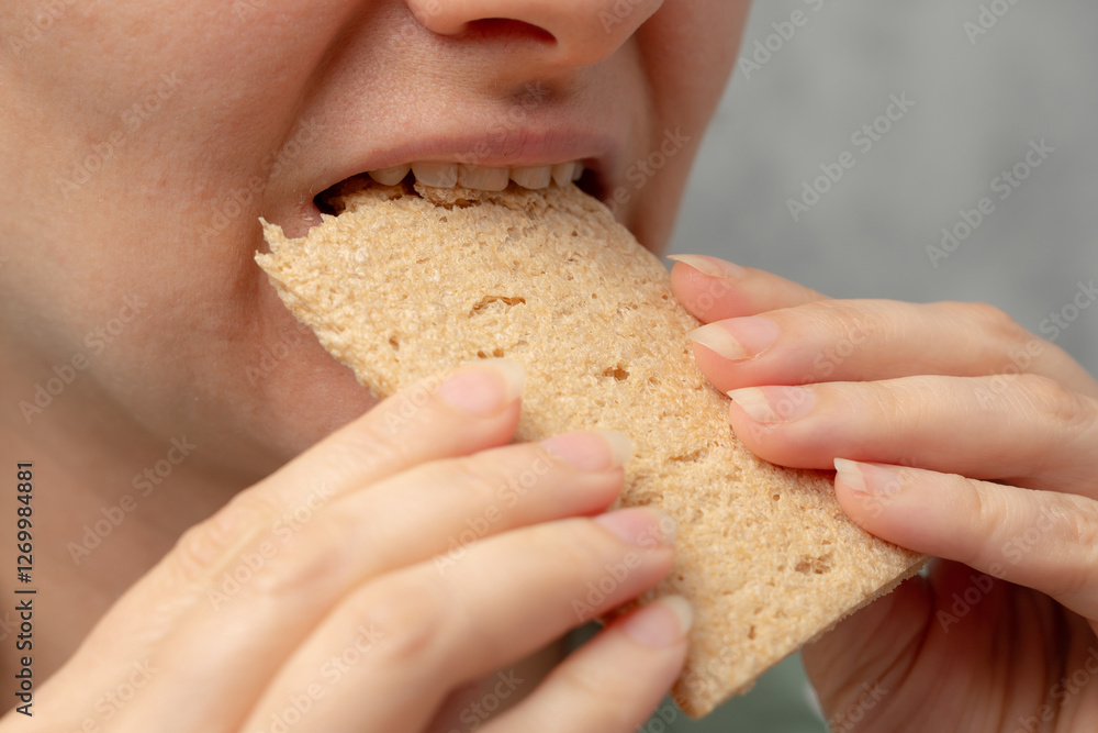 A close-up of a woman biting into a whole grain cracker. A close-up of a woman biting into a whole grain cracker.