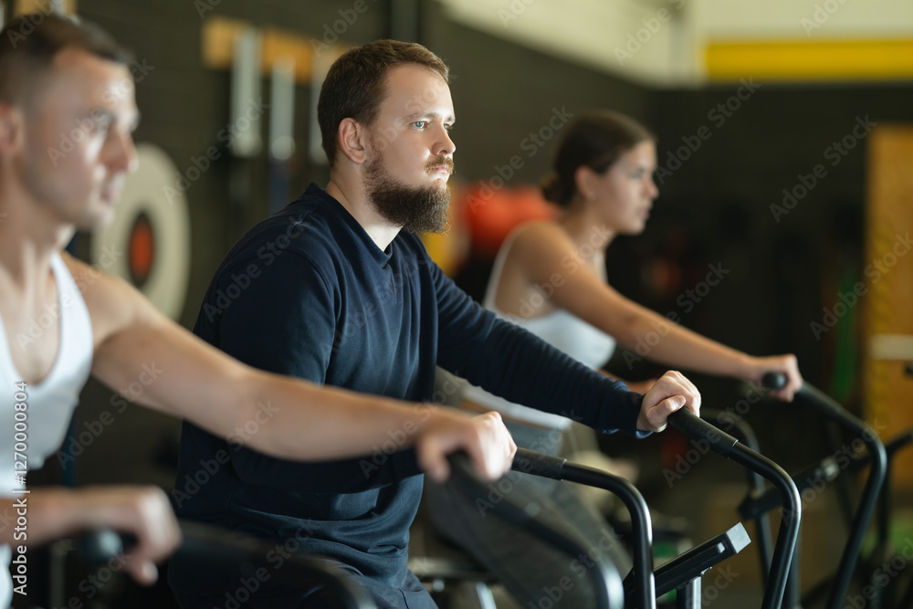 Obraz premium Willing young man engaged in air-bike workout in exercise room during weight training classes