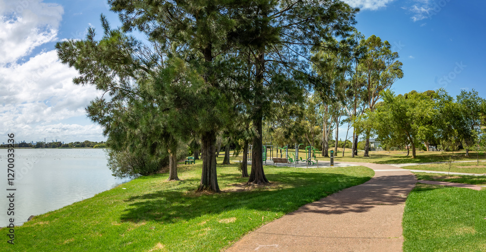 Cherry Lake Park in Altona, featuring a paved pathway curving through lush green parklands alongside the calm lake waters, and an outdoor gym.A suburban recreational outdoor space for local community. Cherry Lake Park in Altona, featuring a paved pathway curving through lush green parklands alongside the calm lake waters, and an outdoor gym.A suburban recreational outdoor space for local community.