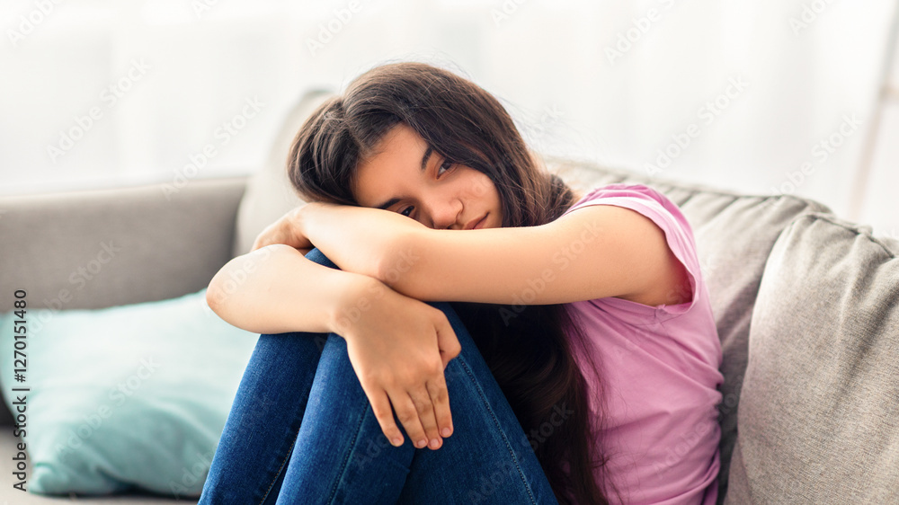 Unhappy teen girl feeling depressed or desperate, sitting on couch at home. Indian asdolescent having difficult times, suffering from problem or teenage depression, indoors Unhappy teen girl feeling depressed or desperate, sitting on couch at home. Indian asdolescent having difficult times, suffering from problem or teenage depression, indoors