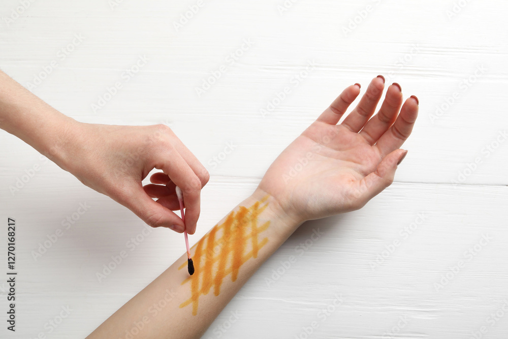 Obraz premium Woman applying topical iodine with cotton swab on hand at white wooden table, top view