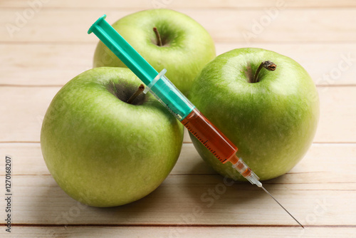 GMO concept. Fresh apples and syringe on wooden table, closeup