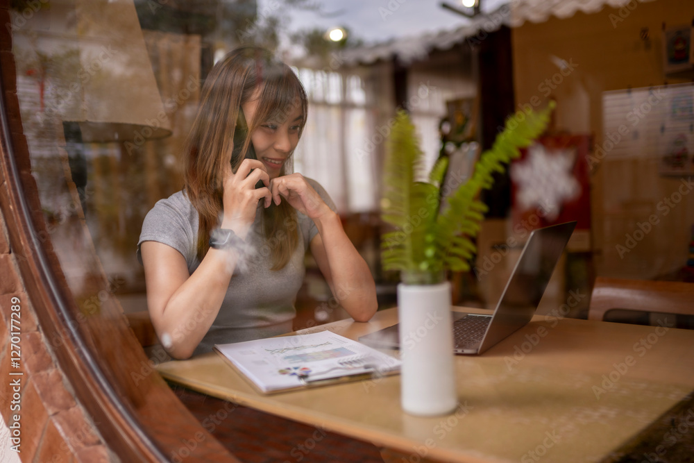 A woman is talking on her cell phone while sitting at a desk with a laptop A woman is talking on her cell phone while sitting at a desk with a laptop