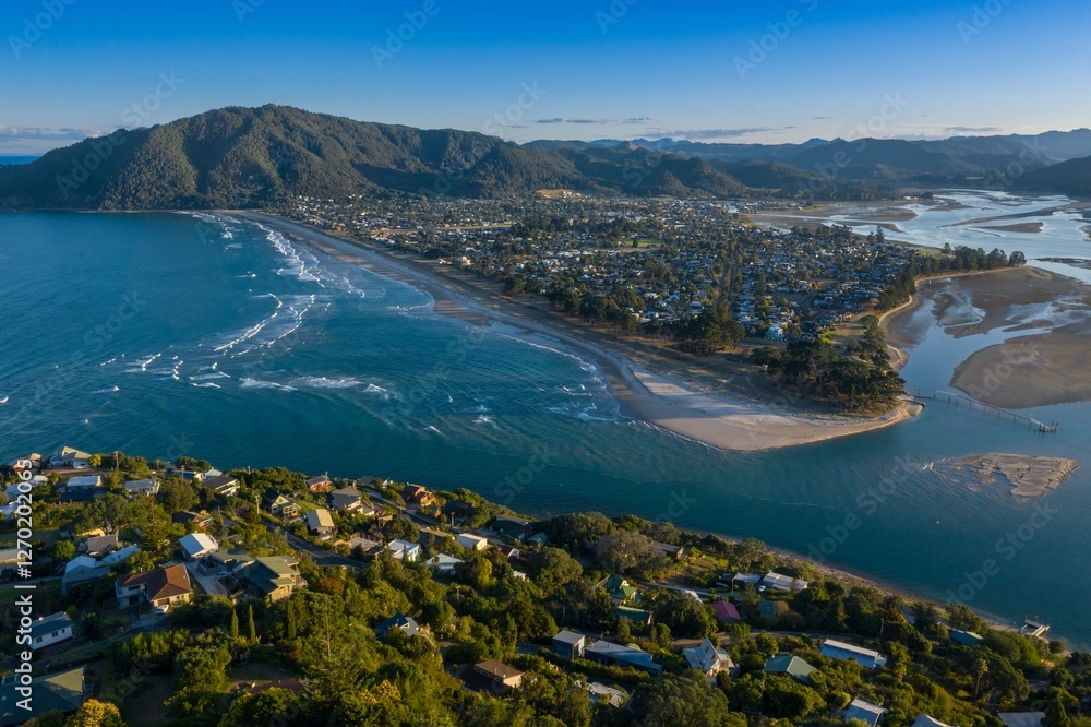 Obraz premium Coastal Pauanui nestled beside a bay, with homes lining the shore and a sandy beach. Aerial view of a tranquil seaside community. Tairua, Coromandel Peninsula, New Zealand