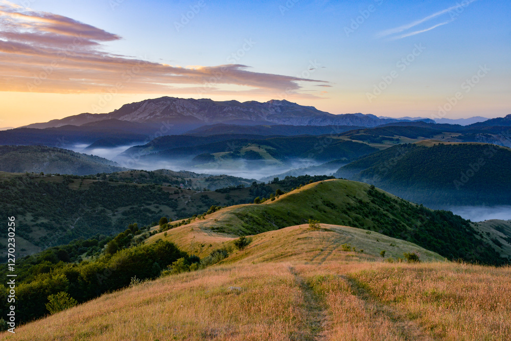 Fototapeta premium Mountain landscape with grassy hills forest and morning fog Sunrise sky adding color to the scene