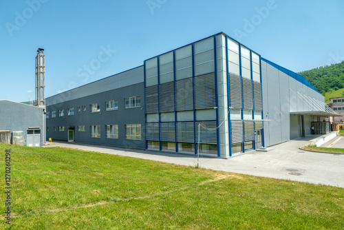 Large industrial building with gray and blue exterior under a bright blue sky surrounded by green grass