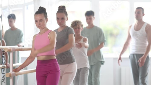 Slim adolescent attendees of ballet courses training battement tendu position under control of ballet-master in dancehall