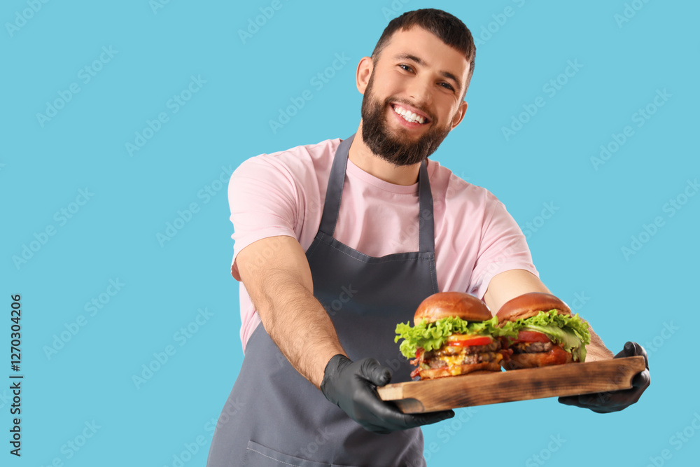 Young male chef holding wooden tray with tasty burgers on blue background Young male chef holding wooden tray with tasty burgers on blue background