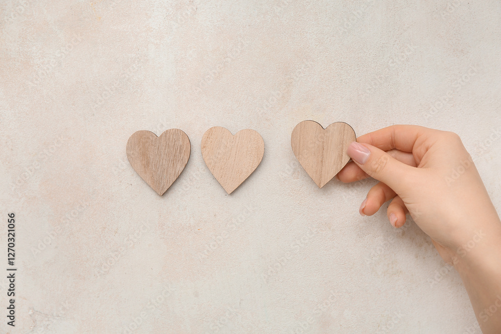 Obraz premium Woman hand placing wooden heart shapes on neutral pastel background, minimalist love concept with copy space, top view