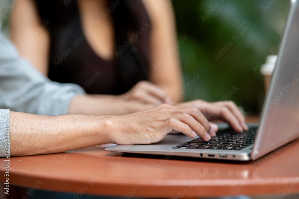 A close-up of a man typing on a laptop keyboard, working on his laptop, sitting at an outdoor table. A close-up of a man typing on a laptop keyboard, working on his laptop, sitting at an outdoor table.