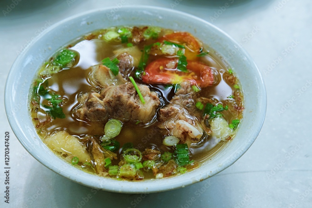 Close-up of Sop Iga, a flavorful Indonesian oxtail soup served in a bowl with tender beef ribs, rich broth, fresh tomatoes, green onions, fried shallots, and aromatic spices. Close-up of Sop Iga, a flavorful Indonesian oxtail soup served in a bowl with tender beef ribs, rich broth, fresh tomatoes, green onions, fried shallots, and aromatic spices.