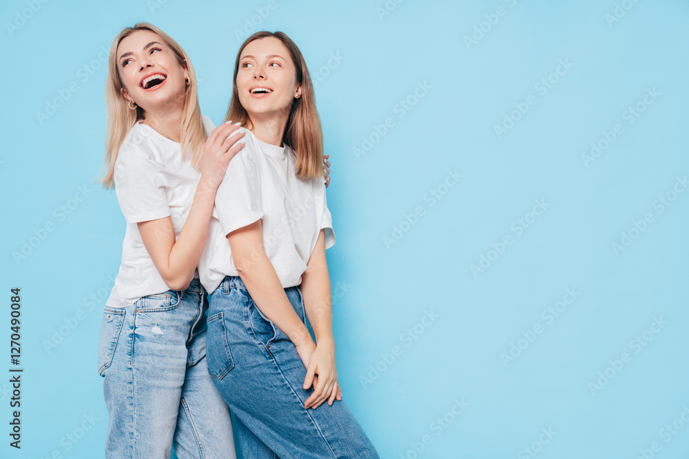 Two young beautiful smiling brunette and blond hipster female in trendy summer clothes. Lovely women posing on blue background in studio. Positive models having fun. Cheerful and happy. isolated Two young beautiful smiling brunette and blond hipster female in trendy summer clothes. Lovely women posing on blue background in studio. Positive models having fun. Cheerful and happy. isolated