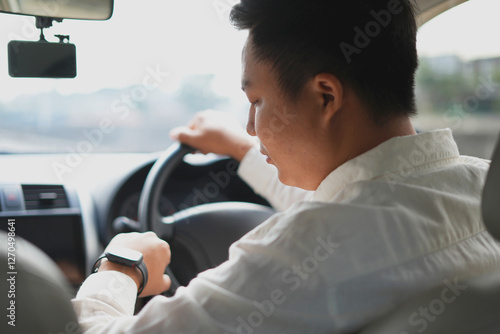 An asian business man using smart phone in the middle of traffic, looking at the watch as he is too late for the meeting, and drinking the morning coffee, driving on highway, usual traffic in city.