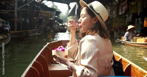 Young Asian tourist woman cheerful and happy to eat street food and sight seeing travel by boat along the canel at Damnoen Saduak Floating Market Thailand