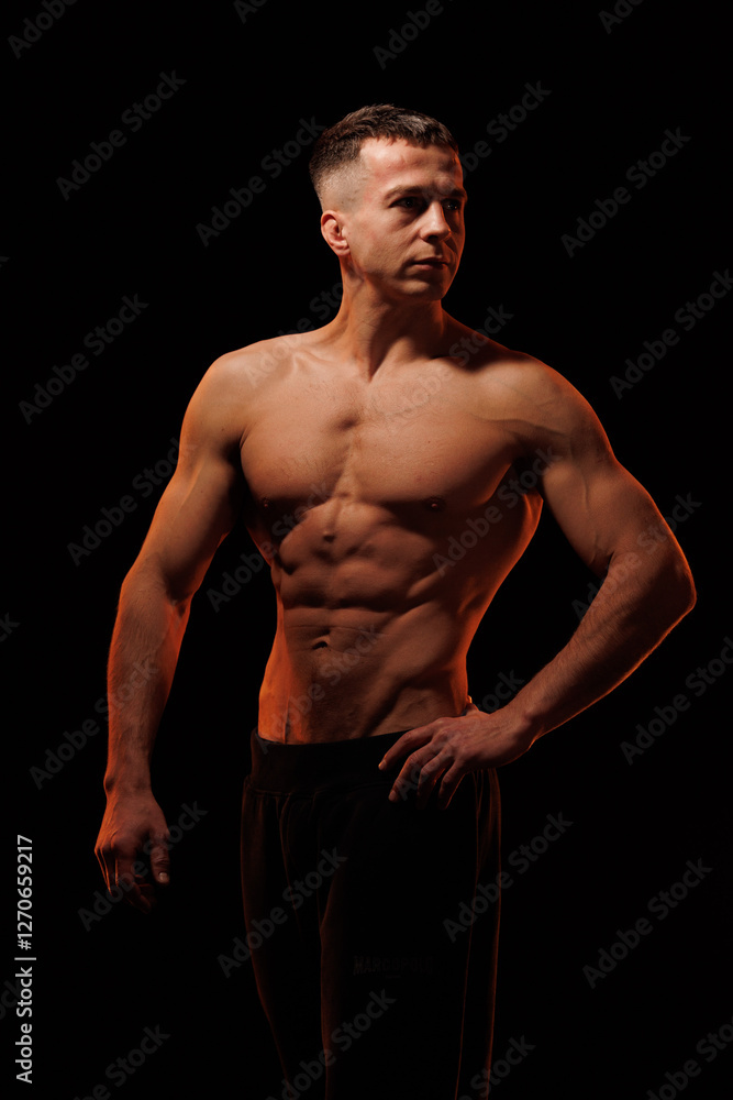 Fototapeta premium Adult male athlete bodybuilder posing on a orange light