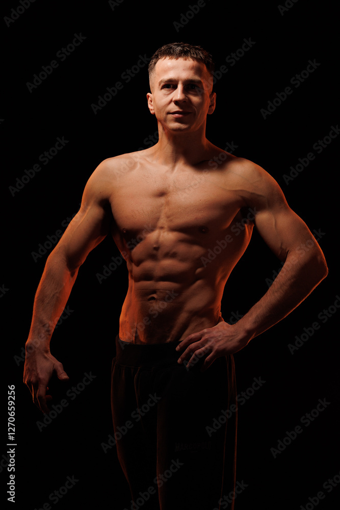 Fototapeta premium Adult male athlete bodybuilder posing on a orange light